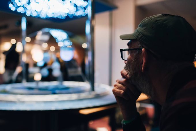 A bearded man in glasses and a green cap studying a lit flat Earth model display at the convention