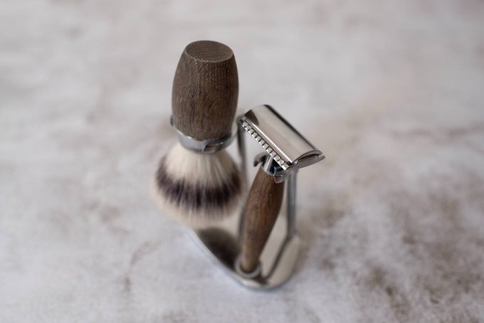 A safety razor and shaving brush with matching wooden handles resting together in a chrome stand