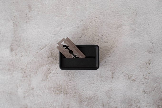 An Astra Superior Platinum double-edge razor blade resting on top of a black blade disposal tin